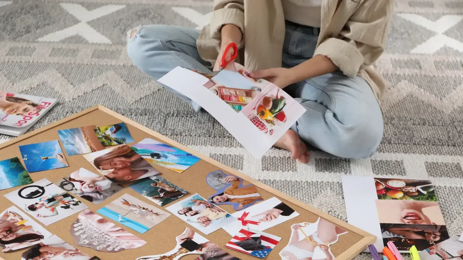 Woman sitting on the floor creating a vision board, cutting out images and arranging them on a board.