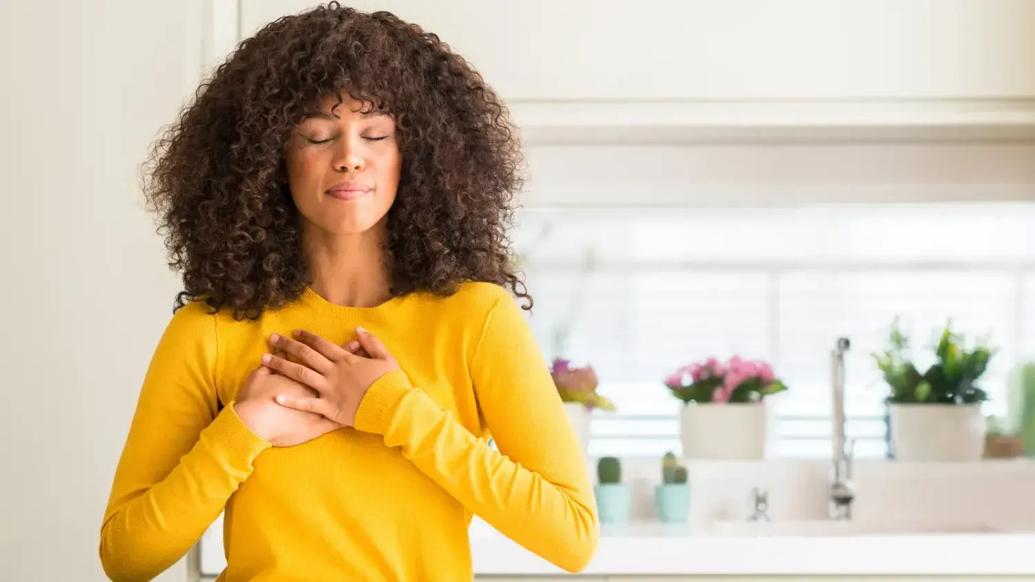 Woman with hands over her heart, practicing gratitude and mindfulness in a bright home setting.