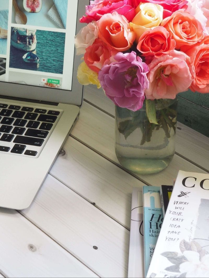 Vase of brightly coloured roses alongside a laptop on a table	