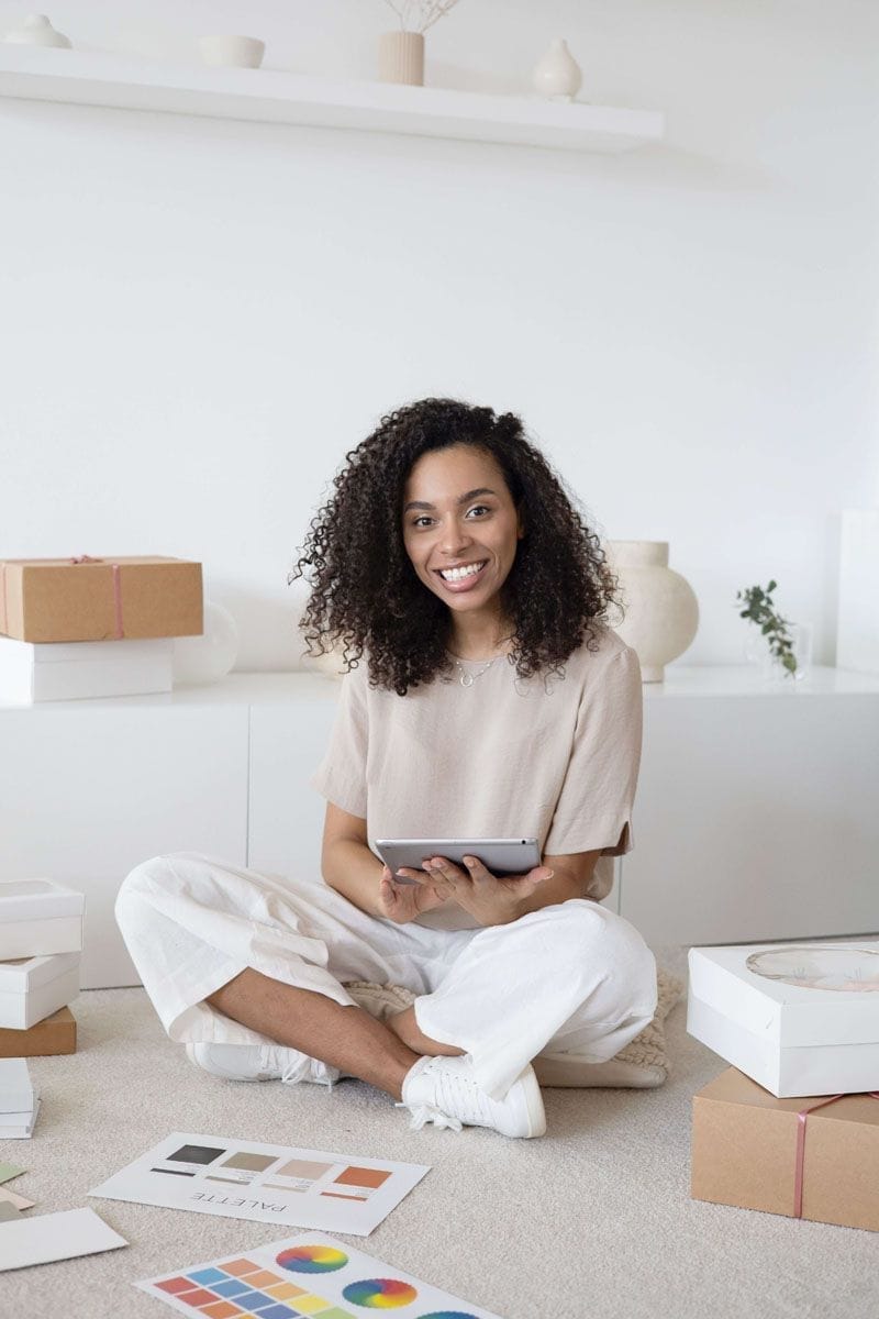 Smiling woman sitting cross legged on the floor surrounded by colour swatches	