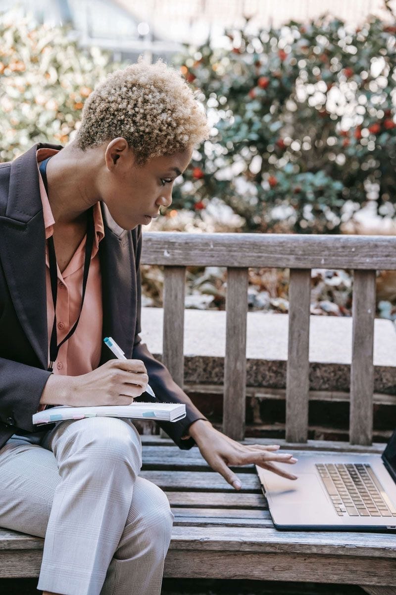 Business woman sitting on an outside bench working on a laptop	