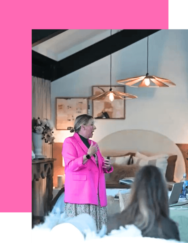 Justine McLean, a woman with blond hair tied back, wearing a bright pink jacket, speaking to a room of women.	