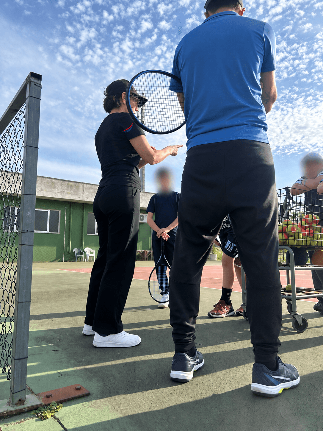 Simona Quarta sul campo da tennis con un allenatore e giovani atleti; volti dei ragazzi oscurati