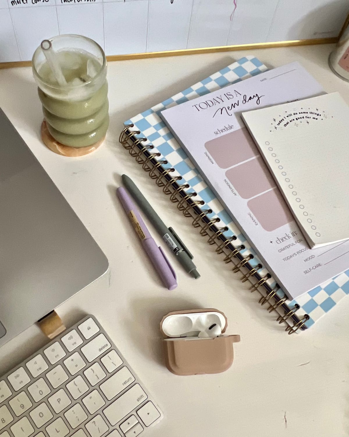desk set up with notepads, keyboard, ear plugs and drink