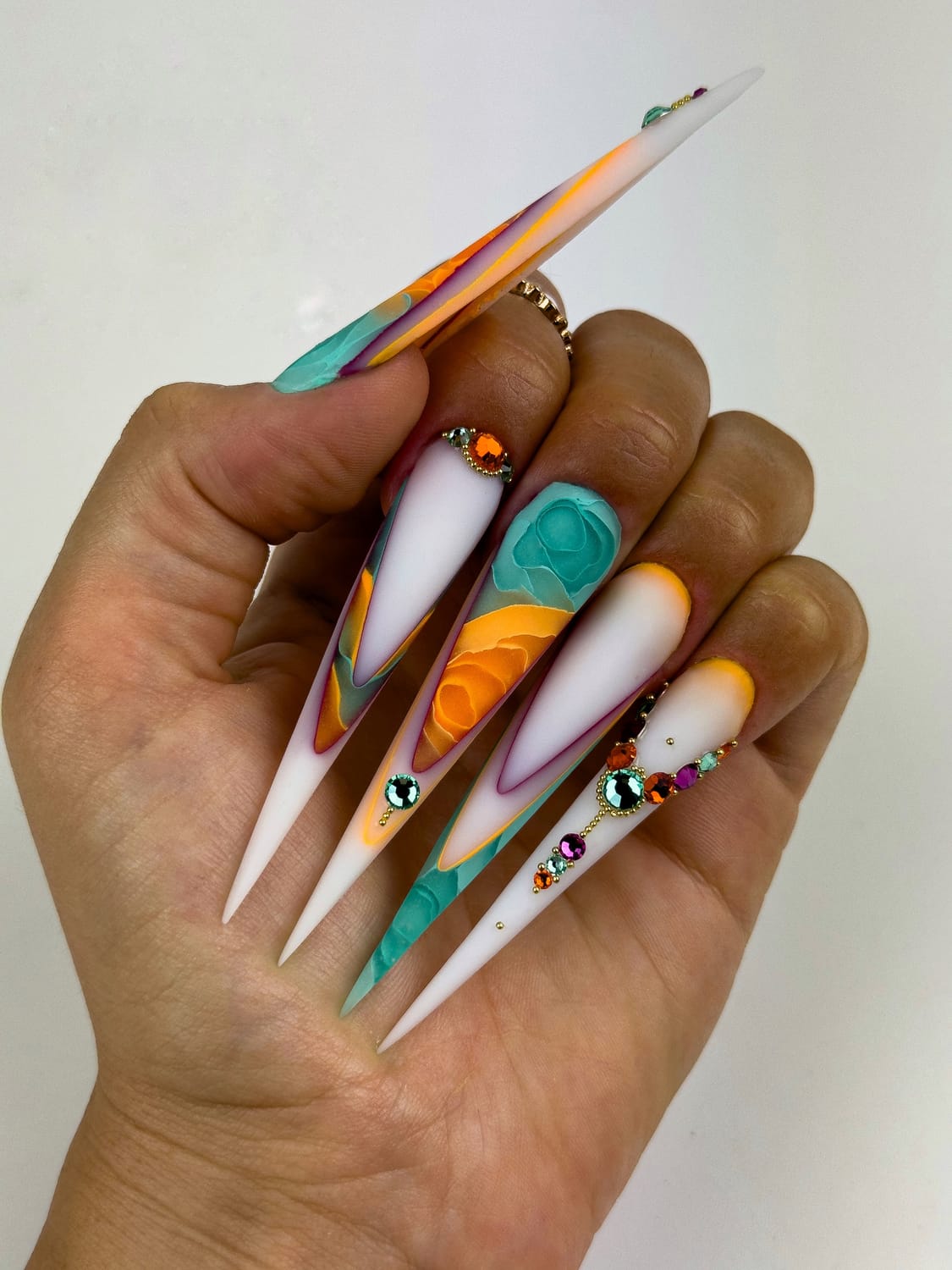 Pose artistique stiletto avec fleurs turquoise et orange, French reverse et bijoux d’ongles