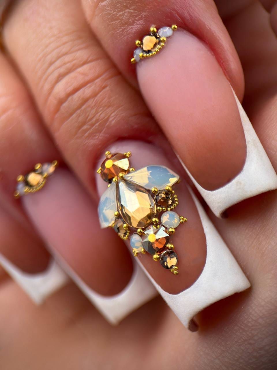 Pose French blanche carrée avec base nude mate et composition de bijoux d’ongles dorés et opalescents