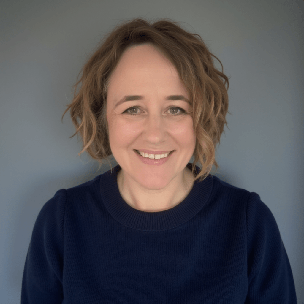 Picture of a woman (Emily Wilkinson) with a maroon jumper. She has short wavy hair and is pictured in front of a wall with a thick vine on it.