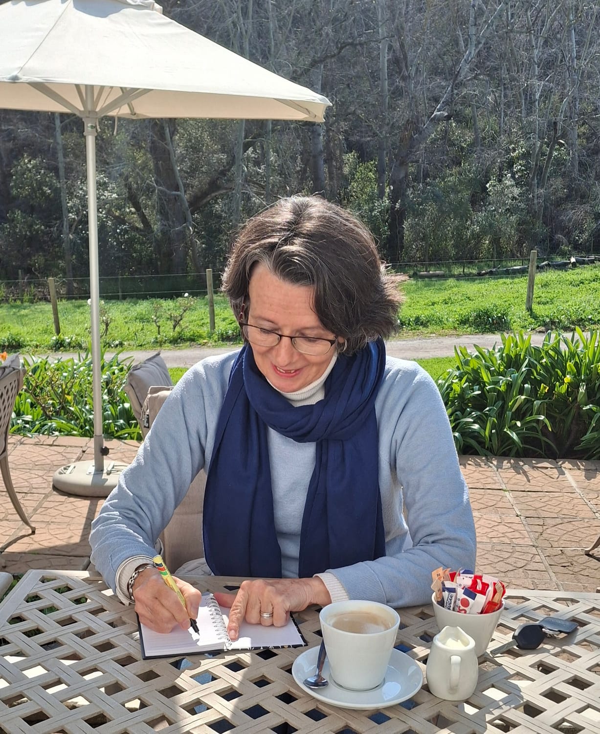 Photo of Milandre Vlok, outside and writing in a book, with acup of coffee.