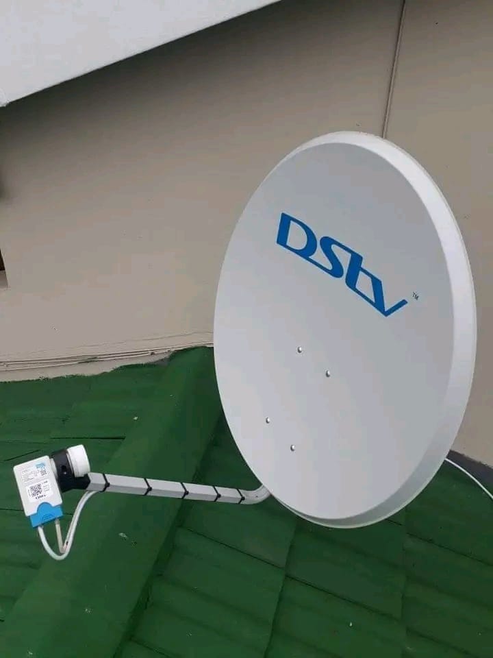 A white DStv satellite dish is mounted on a green-tiled roof, with a clear sky above.