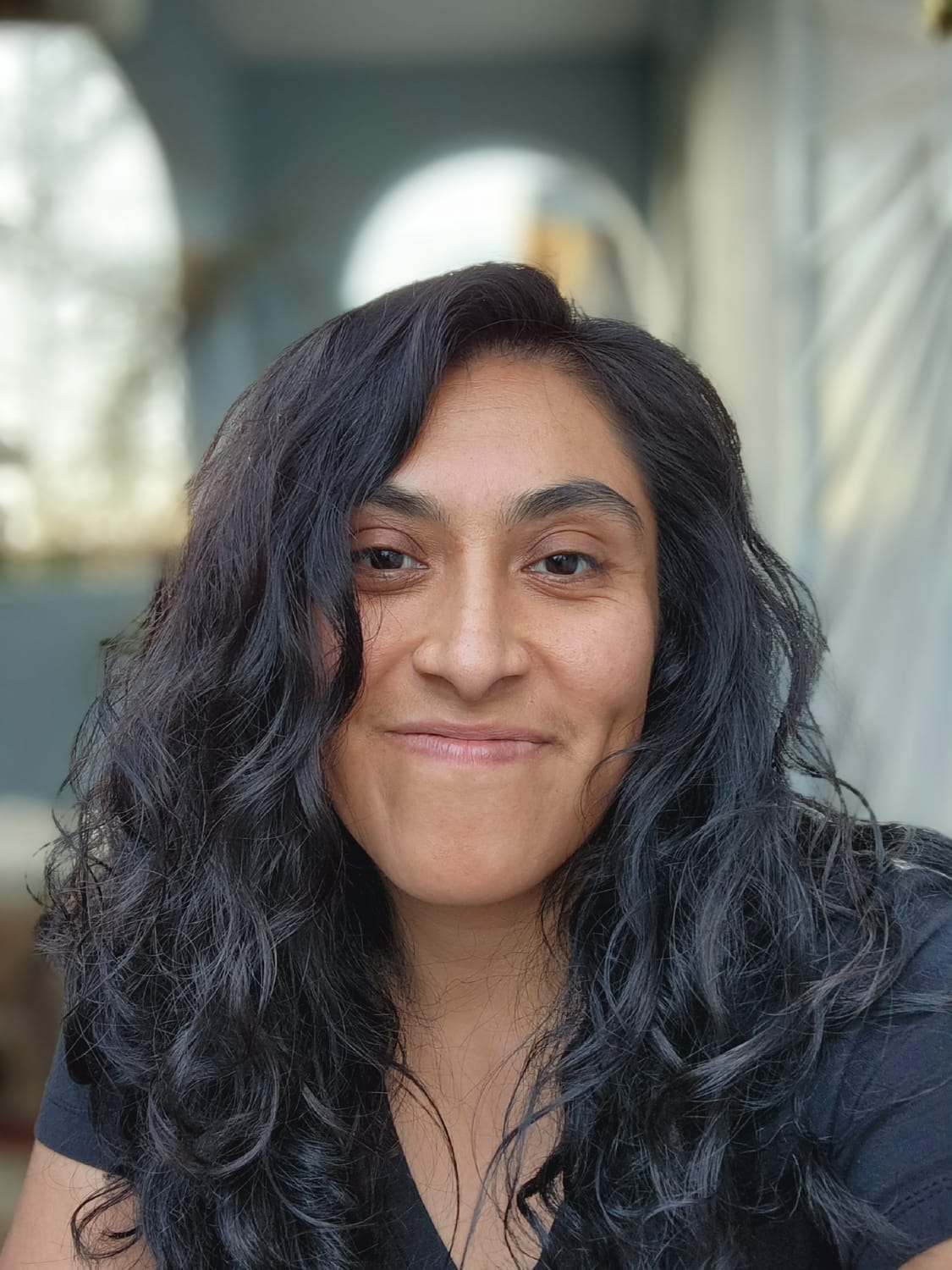 Professional headshot of Fabby, owner of Oakland Hills Pet Care, smiling warmly at the camera with long dark wavy hair, conveying trust and compassion as a fellow pet parent who understands the challenges of balancing work and pet care responsibilities.