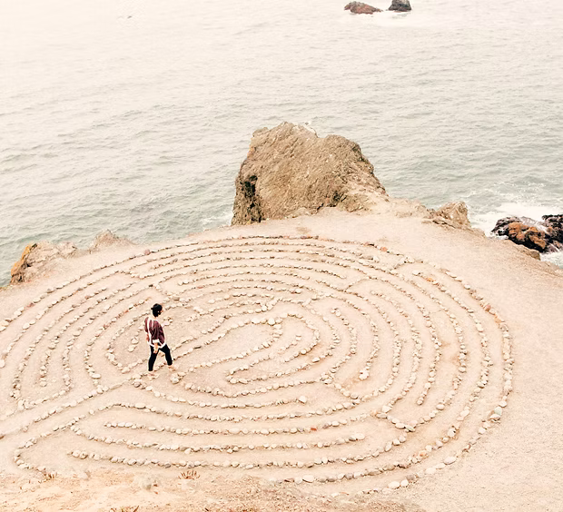 Woman walking through a stone labyrinth on a beach.