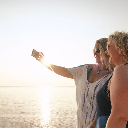 Two women standing together by the water at sunset.