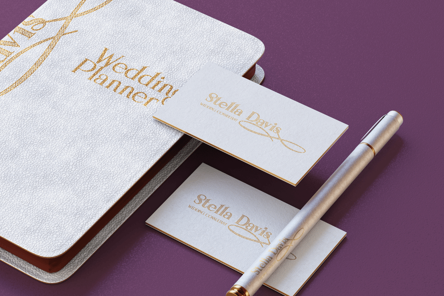 Stationery branding mockup displaying Stella Davis wedding consultant business cards with gold foil lettering, a white textured wedding planner book, and a silver pen on a purple surface.