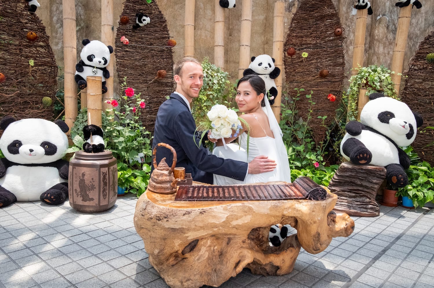 A joyful bi-national couple sitting besides pandas in Hong Kong Park celebrating their marriage.