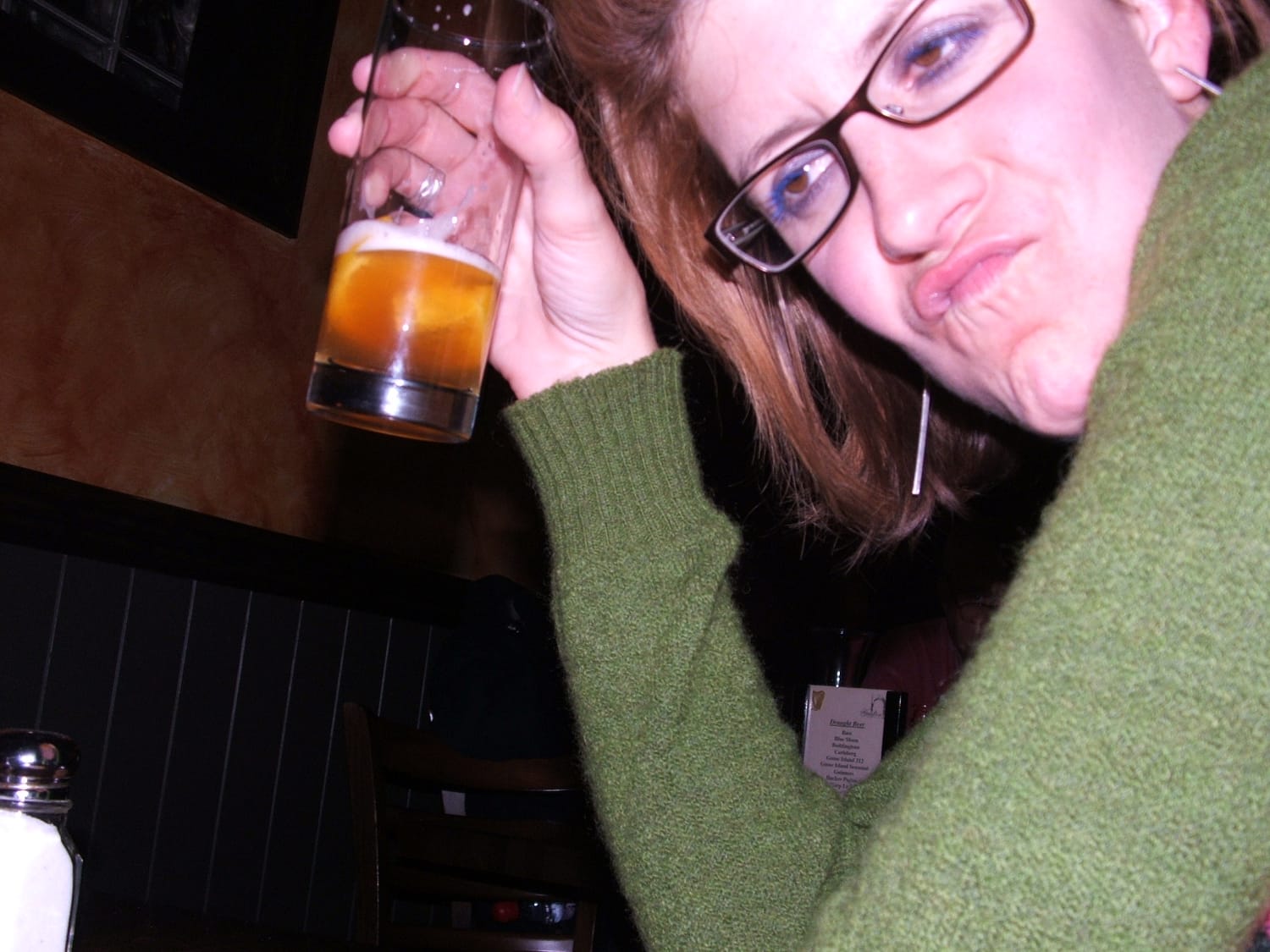 Author in a bar holding a half drunk beer. Her lip is curled up