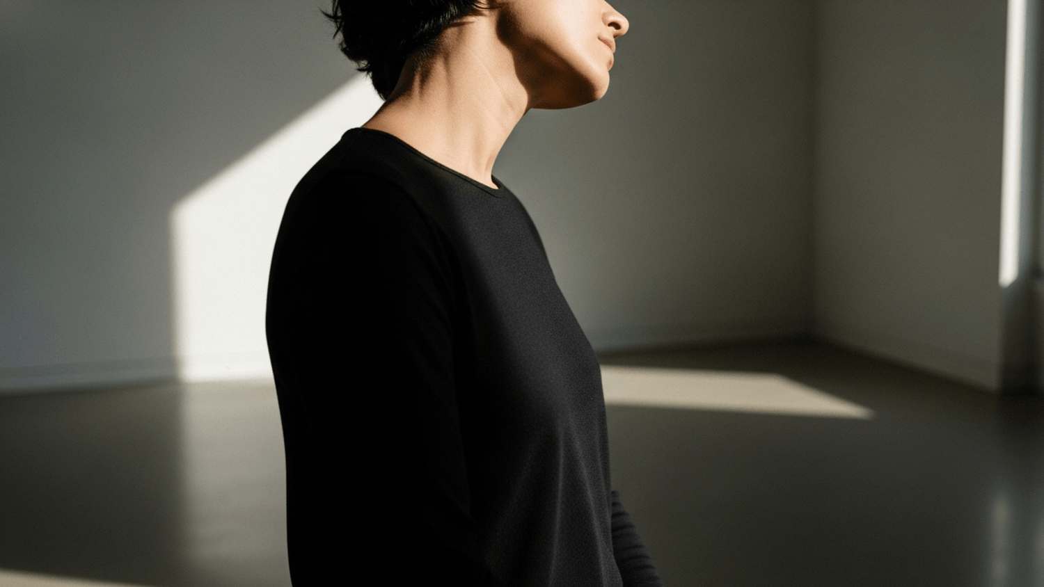 Person gently tilting their neck side to side in a softly lit room to release tension and improve posture