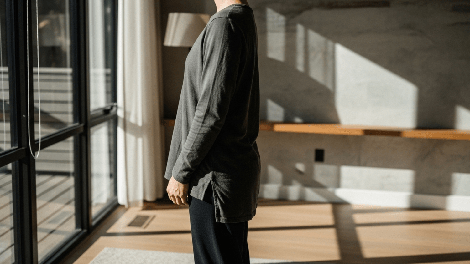 Person standing near a window practicing deep breathing in a softly lit modern room with natural sunlight