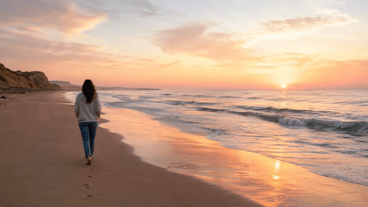 A calm person walking slowly along a quiet beach at sunrise with gentle waves and soft pastel light creating a peaceful atmosphere.