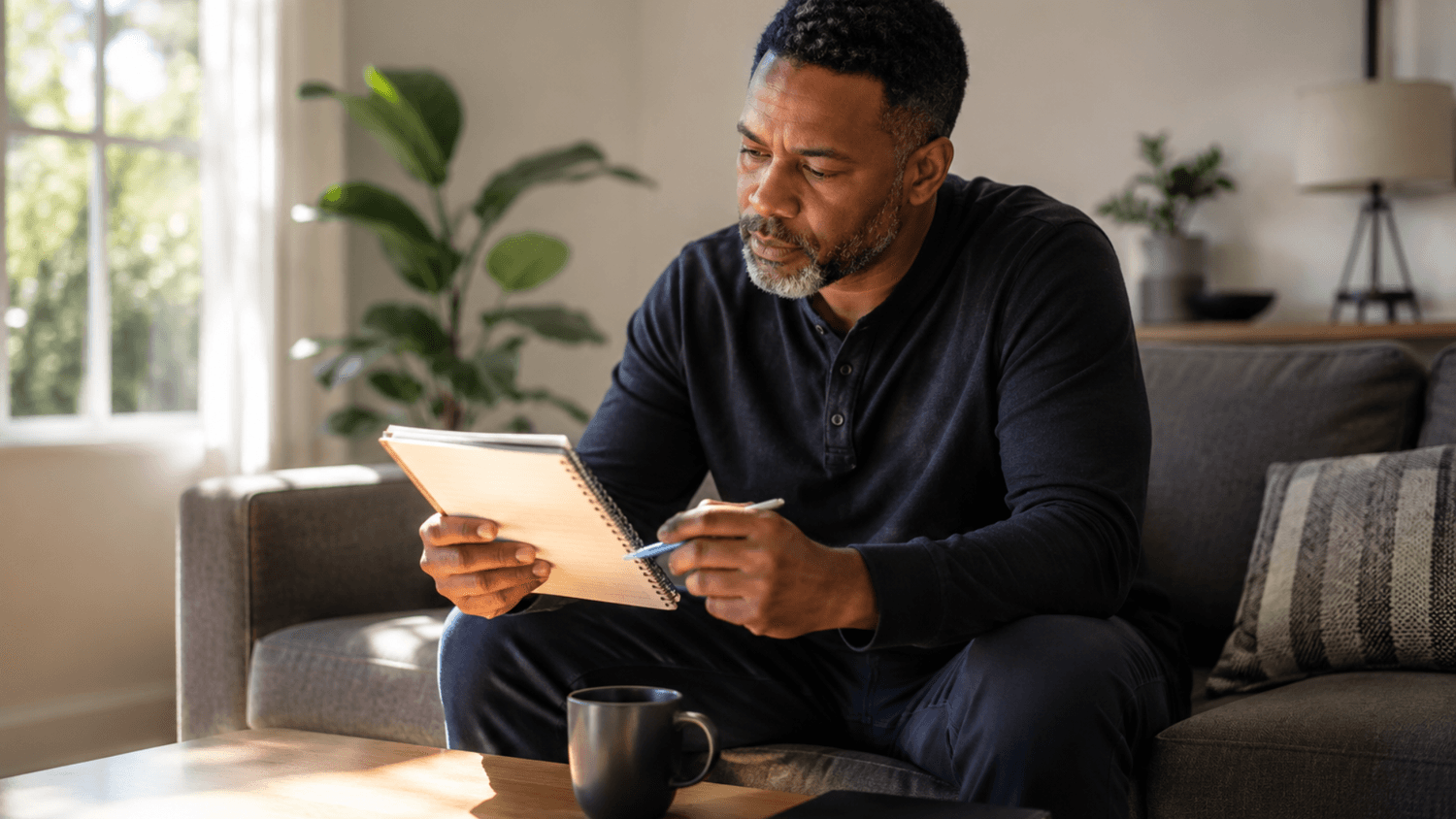Calm individual sitting on a couch reviewing a simple budget notebook in a minimal living space with natural morning light