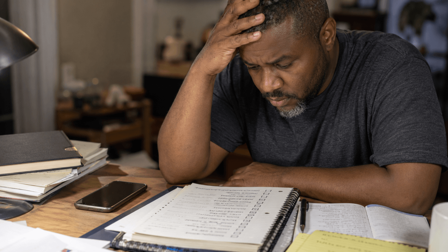 Close-up of a person feeling overwhelmed while looking at a detailed daily routine checklist on a cluttered desk.