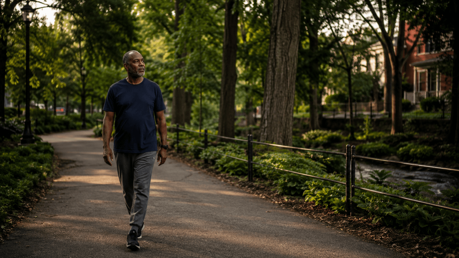 Adult walking attentively along a quiet neighborhood greenway without headphones or a phone.