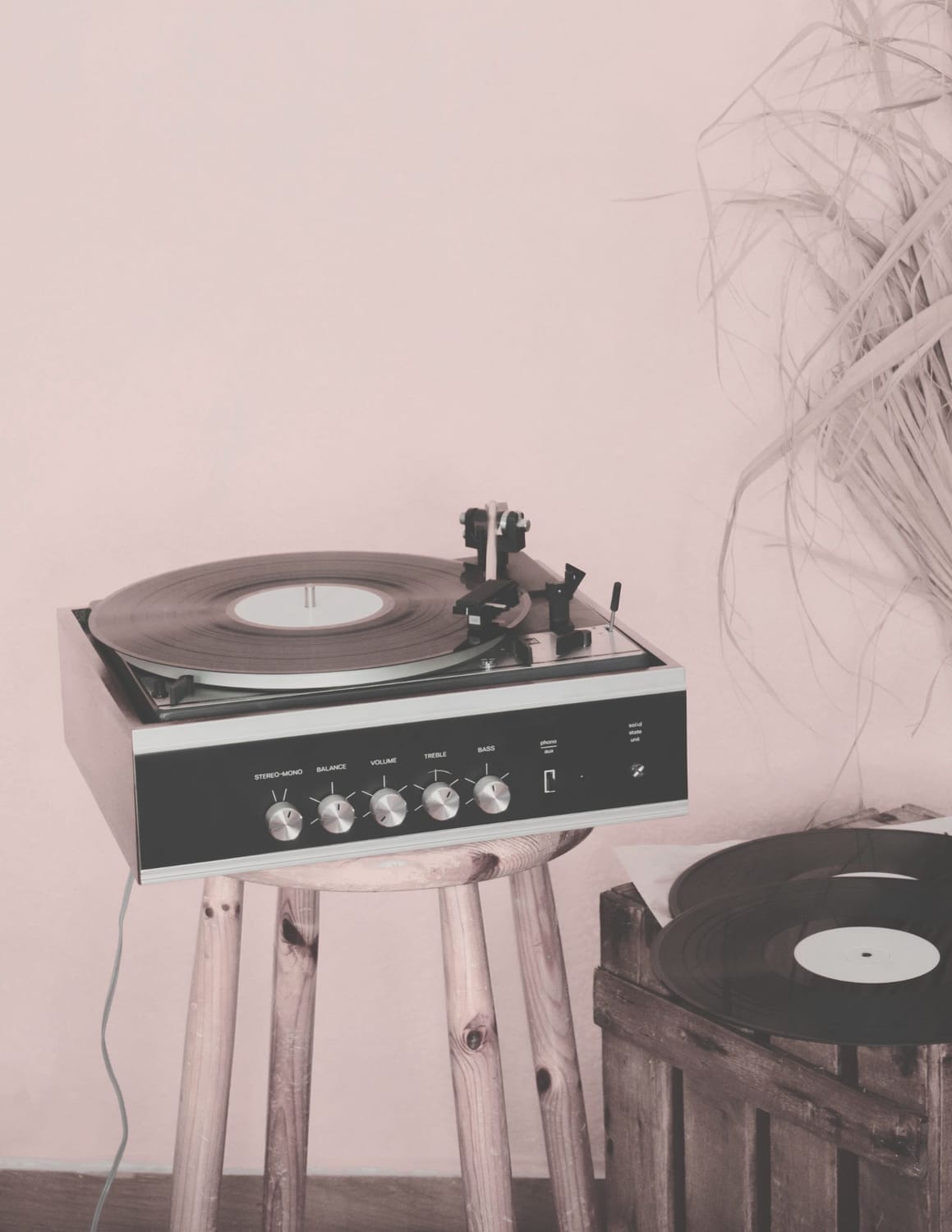 Record player with vinyl on a wooden stool beside a crate of records — warm retro music vibe.