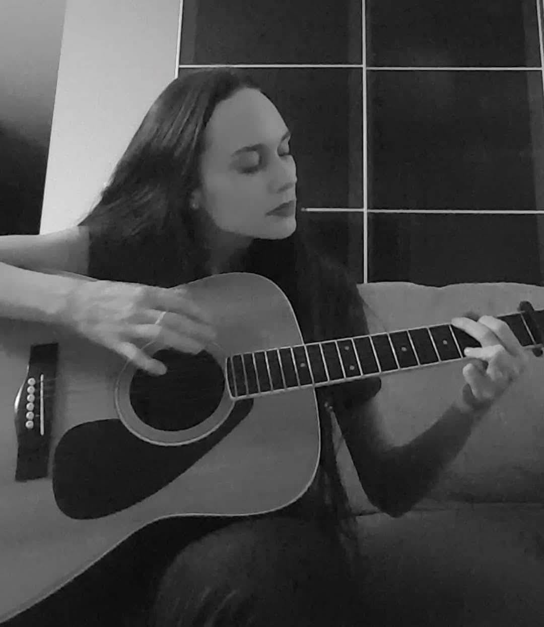 Natalie Jennifer Jones playing acoustic guitar — intimate black-and-white photo highlighting musical creativity and focus.