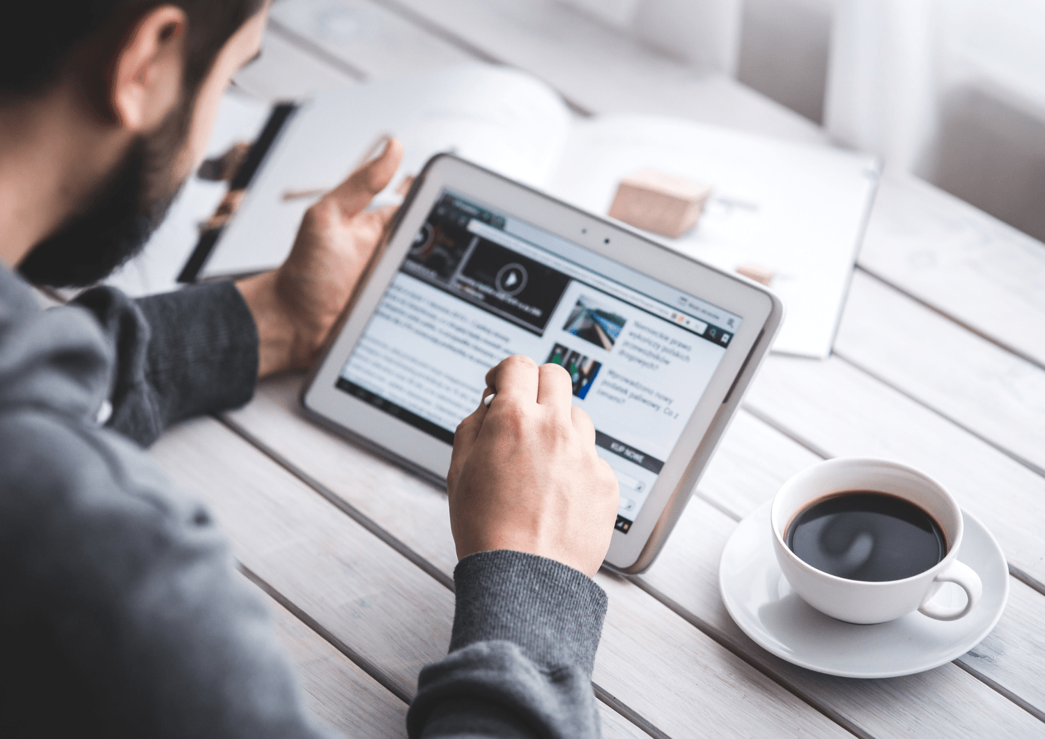Mann som leser en artikkel på nettbrett ved et bord med kaffe – illustrerer konsum av digitalt innhold og blogg