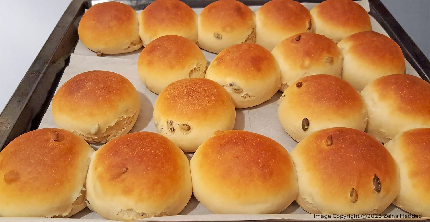 Golden brown yogurt and honey buns seeded with flax and sunflower seeds, arranged on a baking sheet.
