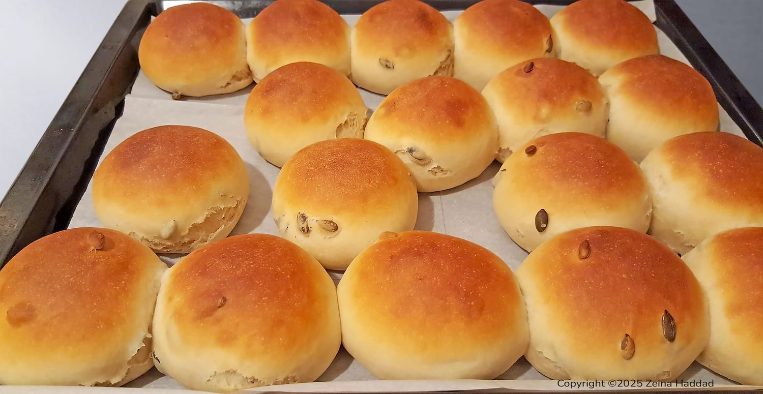 Golden brown yogurt and honey buns seeded with flax and sunflower seeds, arranged on a baking sheet.