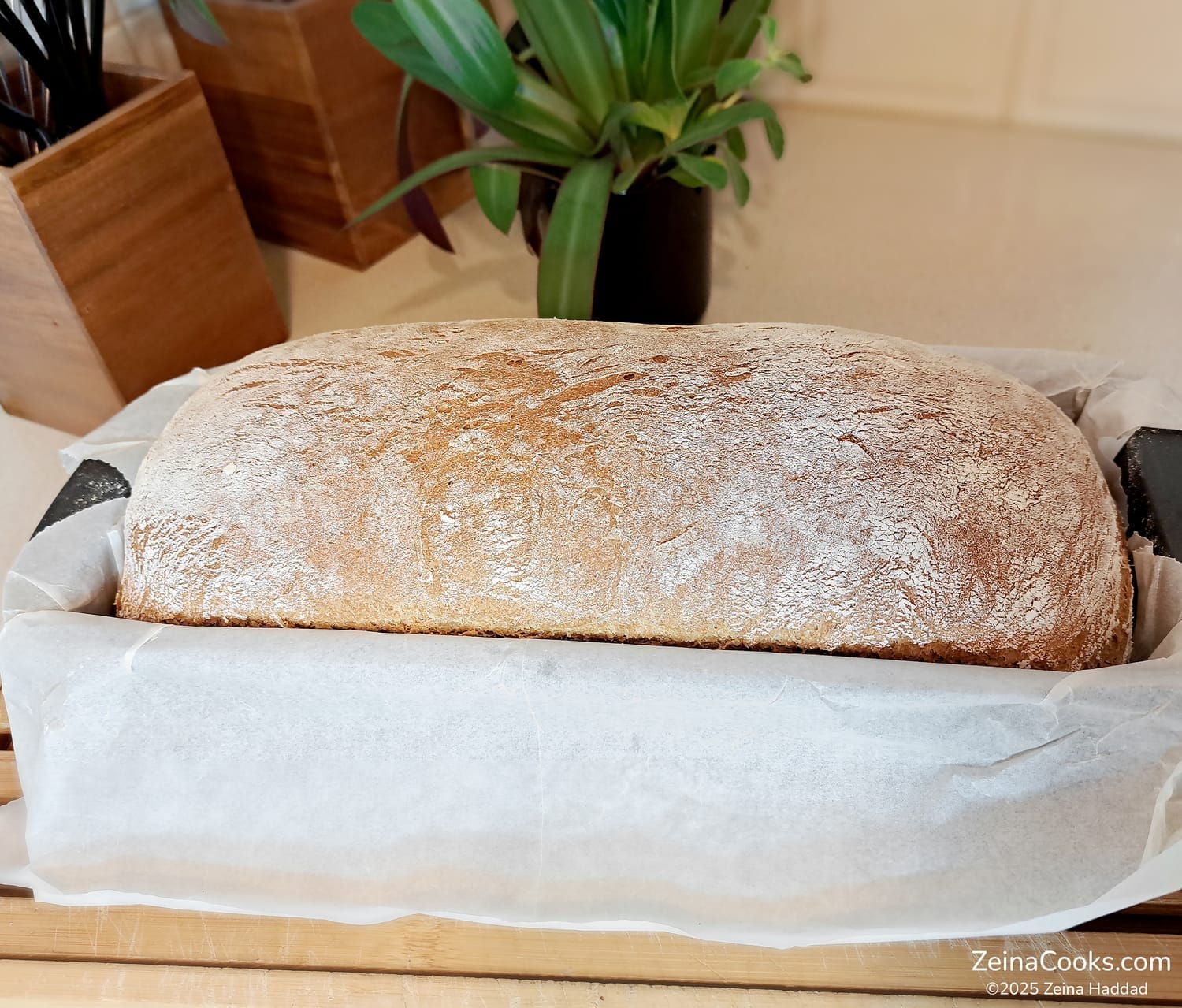 The baked 50/50 Loaf, half white/half wheat flour, with a crispy crust, still in the loaf pan fresh out of the oven, by ZeinaCooks.com.