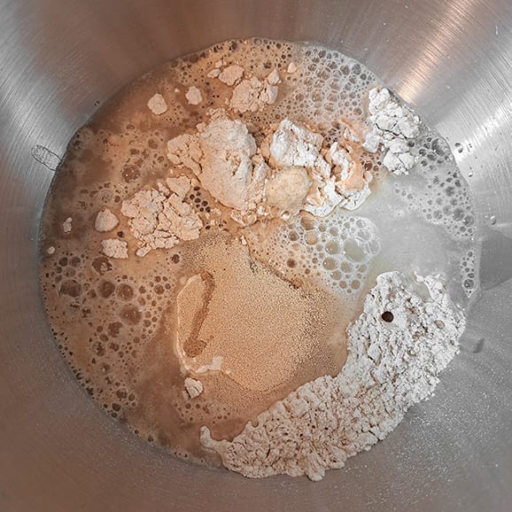 Oil and water added to the dry ingredients in the bowl of a stand mixer for the 50/50 bread loaf by ZeinaCooks.com.