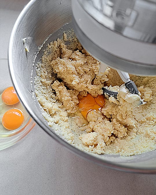 adding eggs to almond flour, powdered sugar, and butter in a stand mixer for almond cream