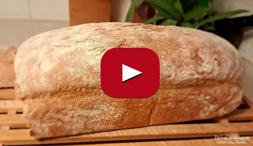 The baked 50/50 Loaf, half white/half wheat flour, with a crispy crust, on a wooden rack, a side view, by ZeinaCooks.com.
