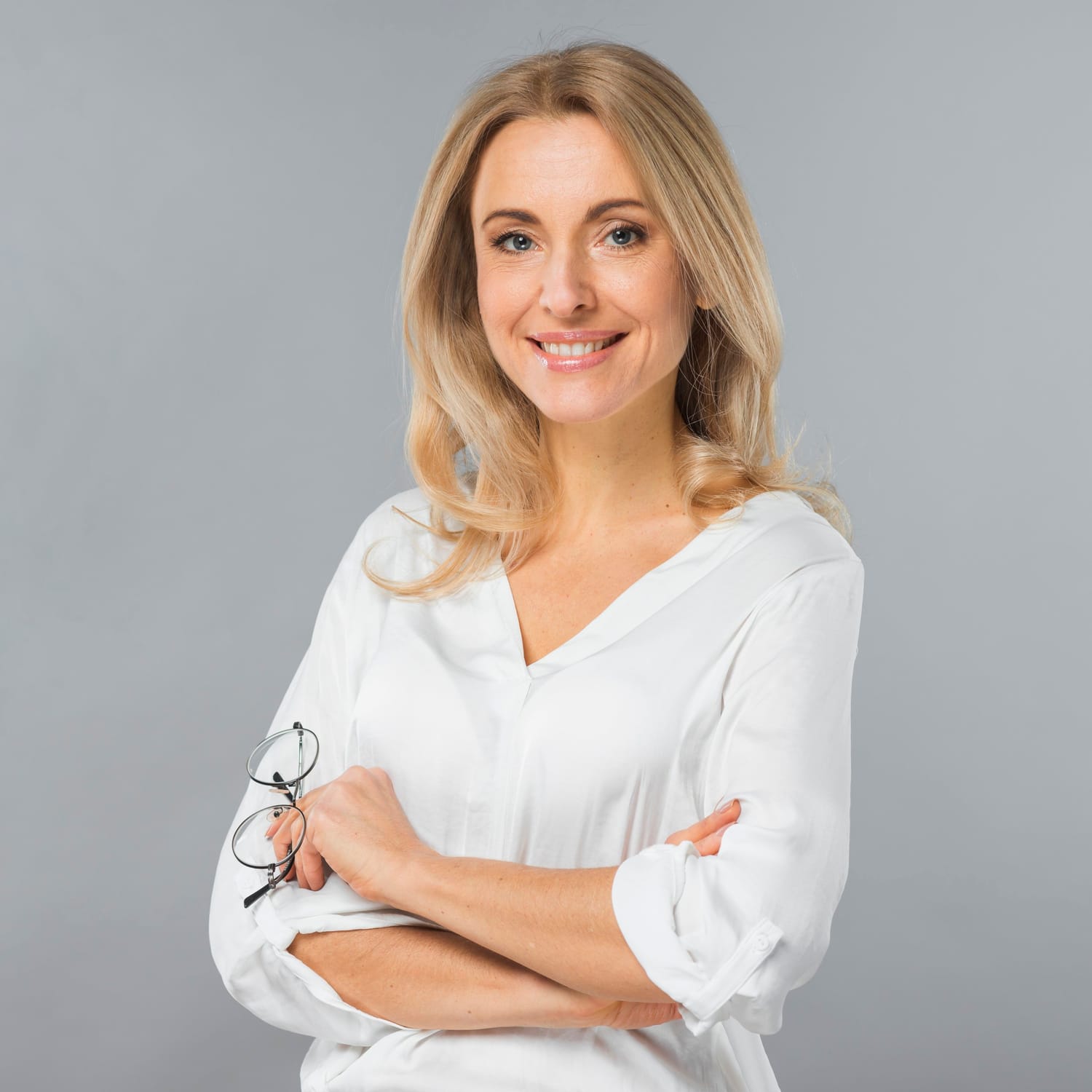 A lady with blonde hair, white blouse, folded arms smiling to camera