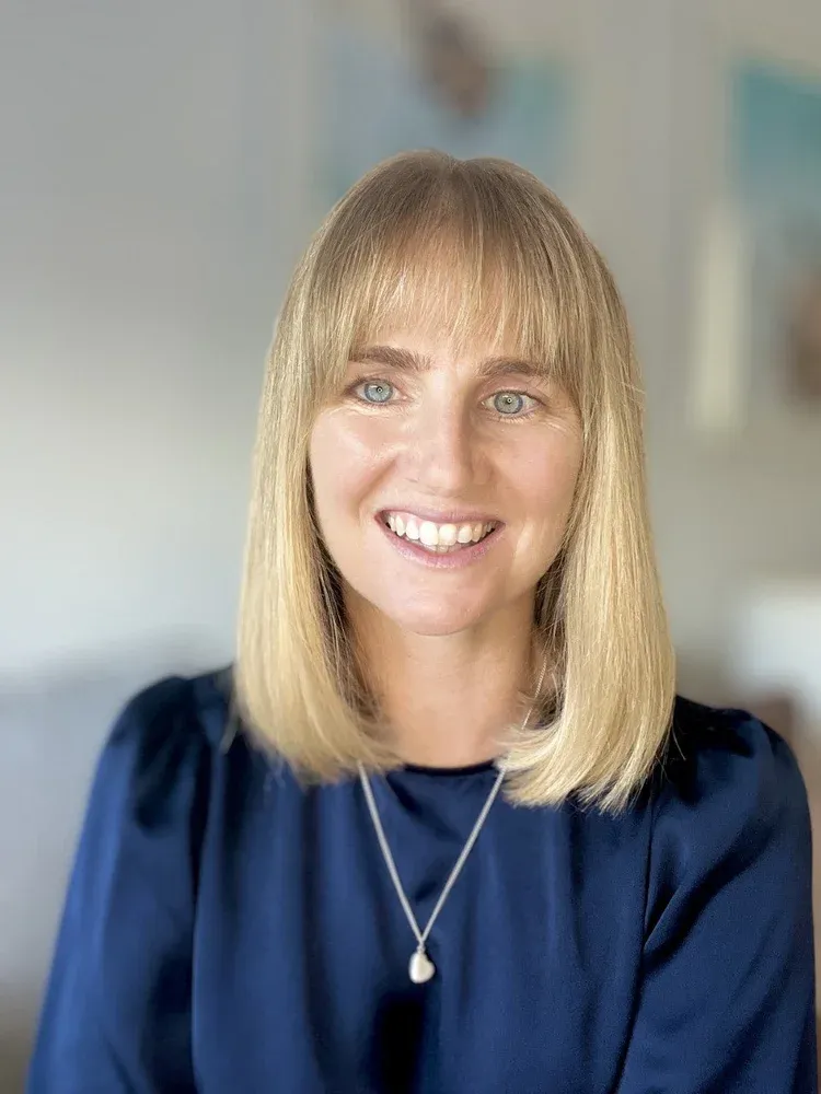 picture of laura thain, navy silk long sleeve top, silver necklace, blonde hair, fringe smiling to camera