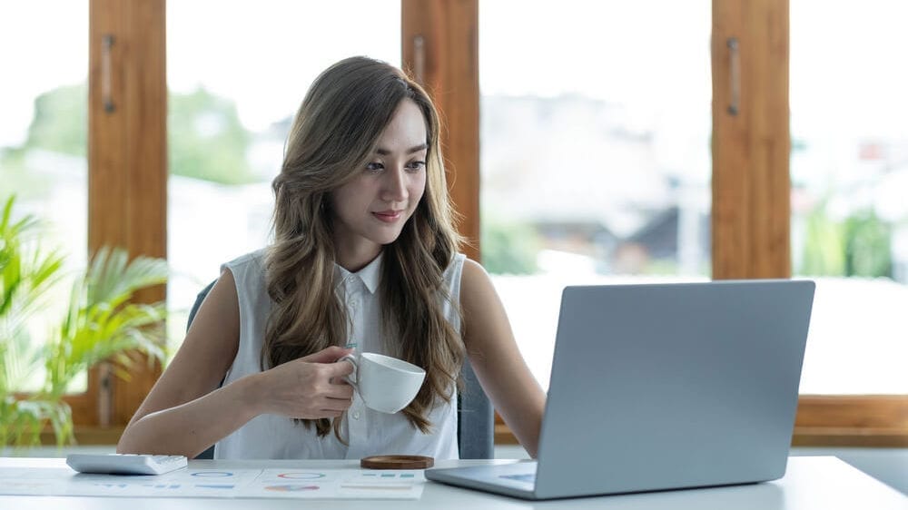 Happy woman working from home on laptop with coffee