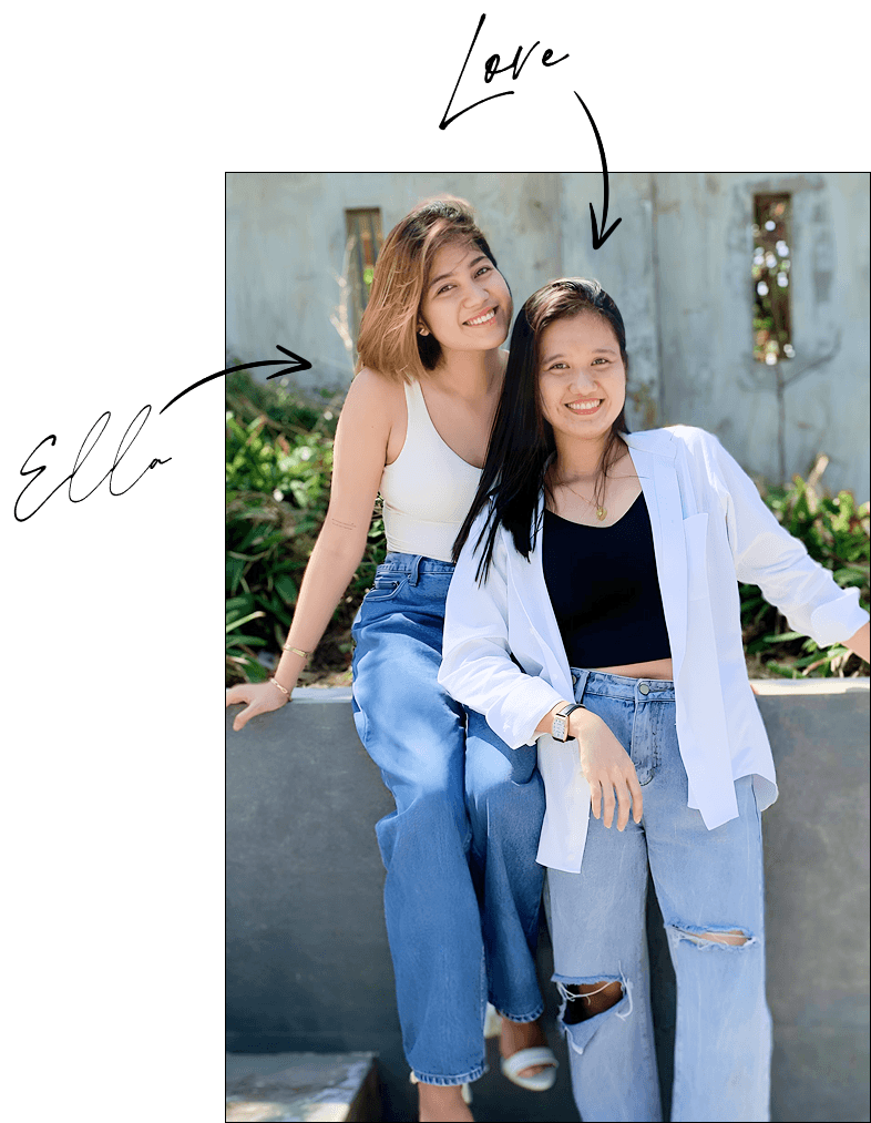 Love and Ella pose outdoors in casual outfits. Ella on the left wears a white sleeveless top and blue jeans, while Love on the right wears a black top, ripped jeans, and a white open shirt. Both are sitting on a ledge in front of greenery and a rustic wall.
