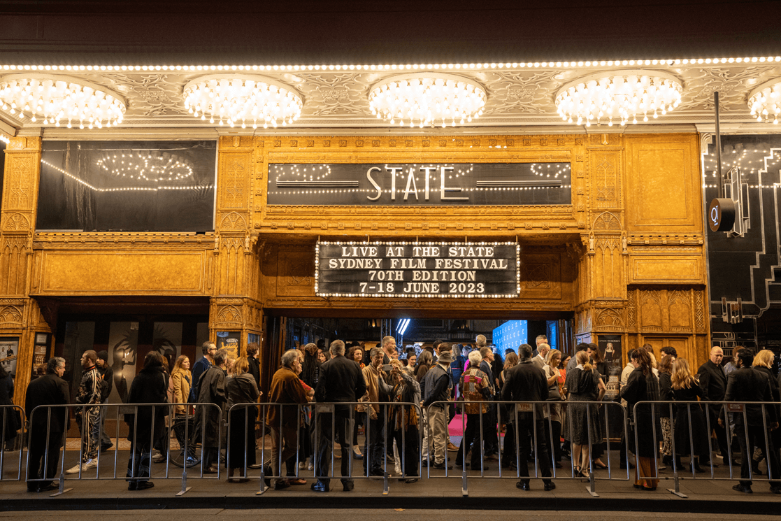 A queue outside a theatre venue with a festival name in lights