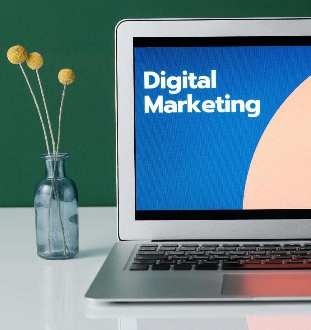 laptop on a desk next to flowers with a screen that says digital marketing