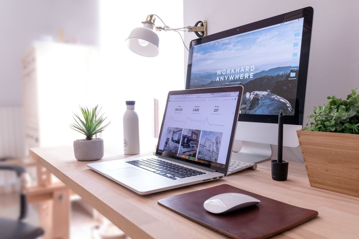 laptop and desktop at a workstation with a mouse, plants, and a lamp