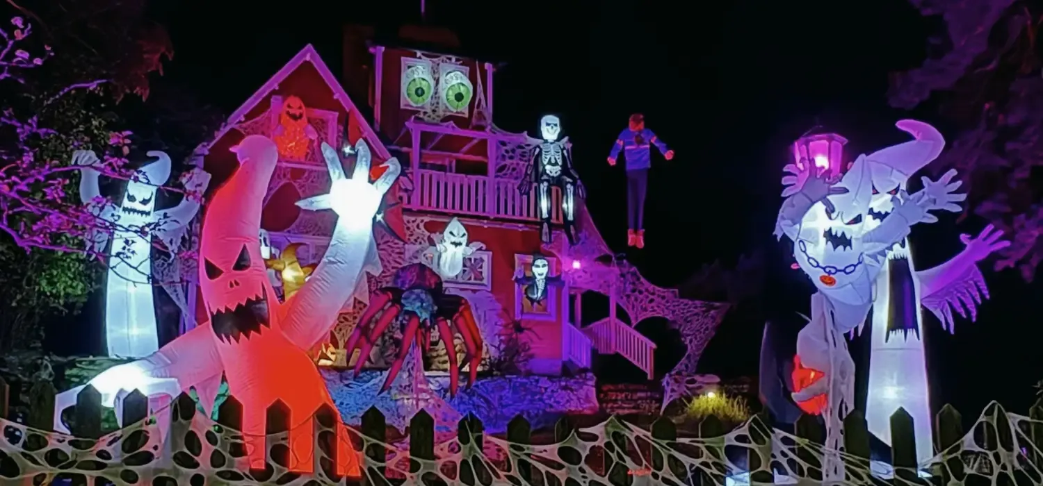 Halloween House i Tyresö – ett upplyst Halloweenhus med spöken, skelett, jättespindel och dekorationer bakom staketet.