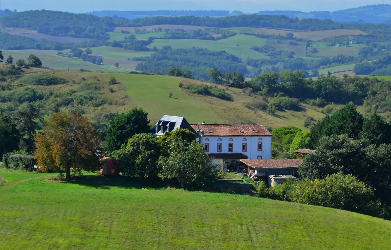 L'écovillage de Pourgues en Ariège : la maison principale au milieu des prés et des collines