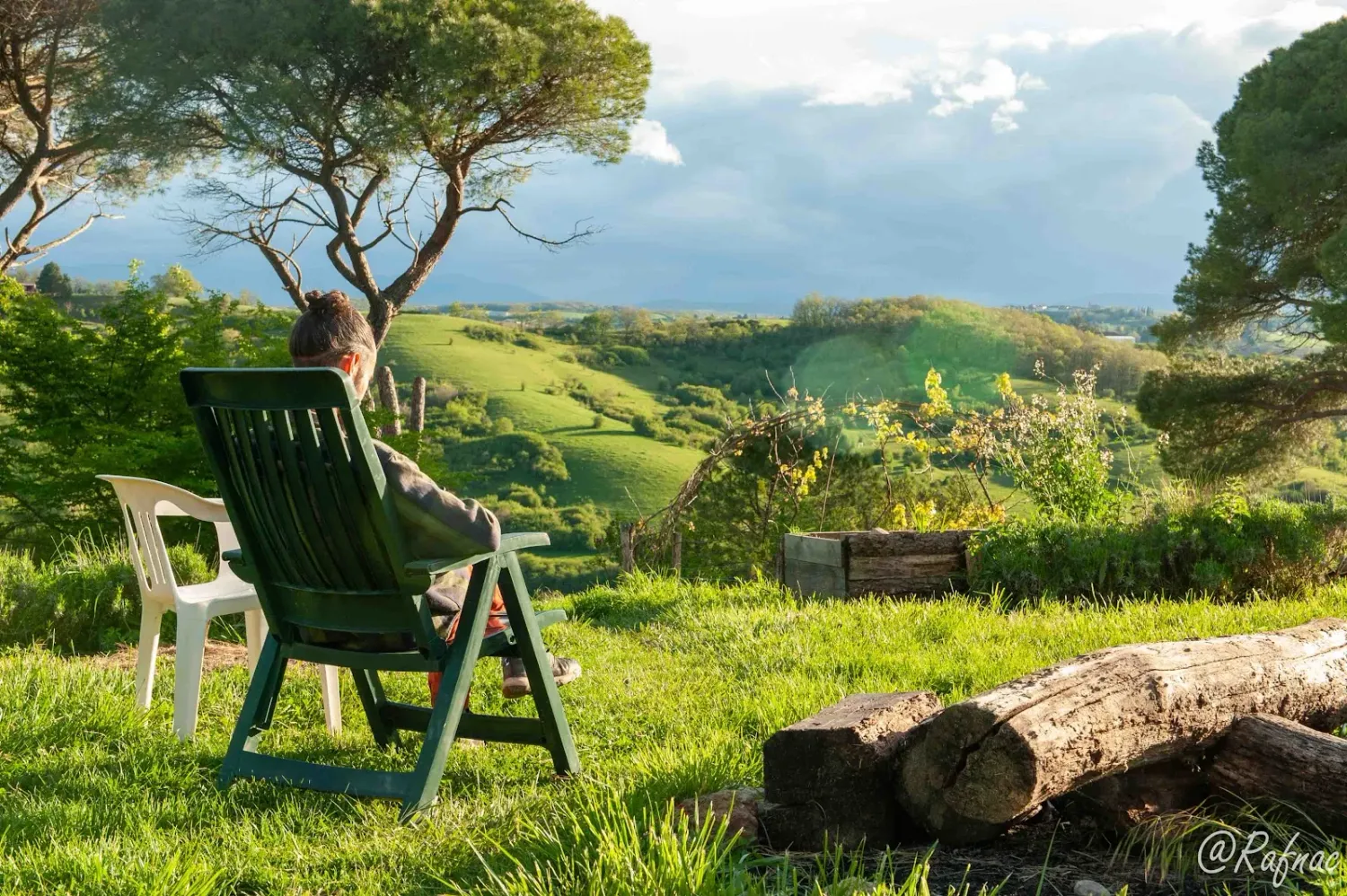 Une personne assise de dos dans une chaise de jardin, face aux collines de l'écovillage de Pourgues