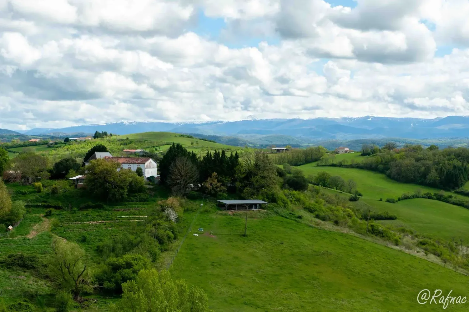 Les bâtiments de l'écovillage de Pourgues vus de loin, au milieu des collines et des prés