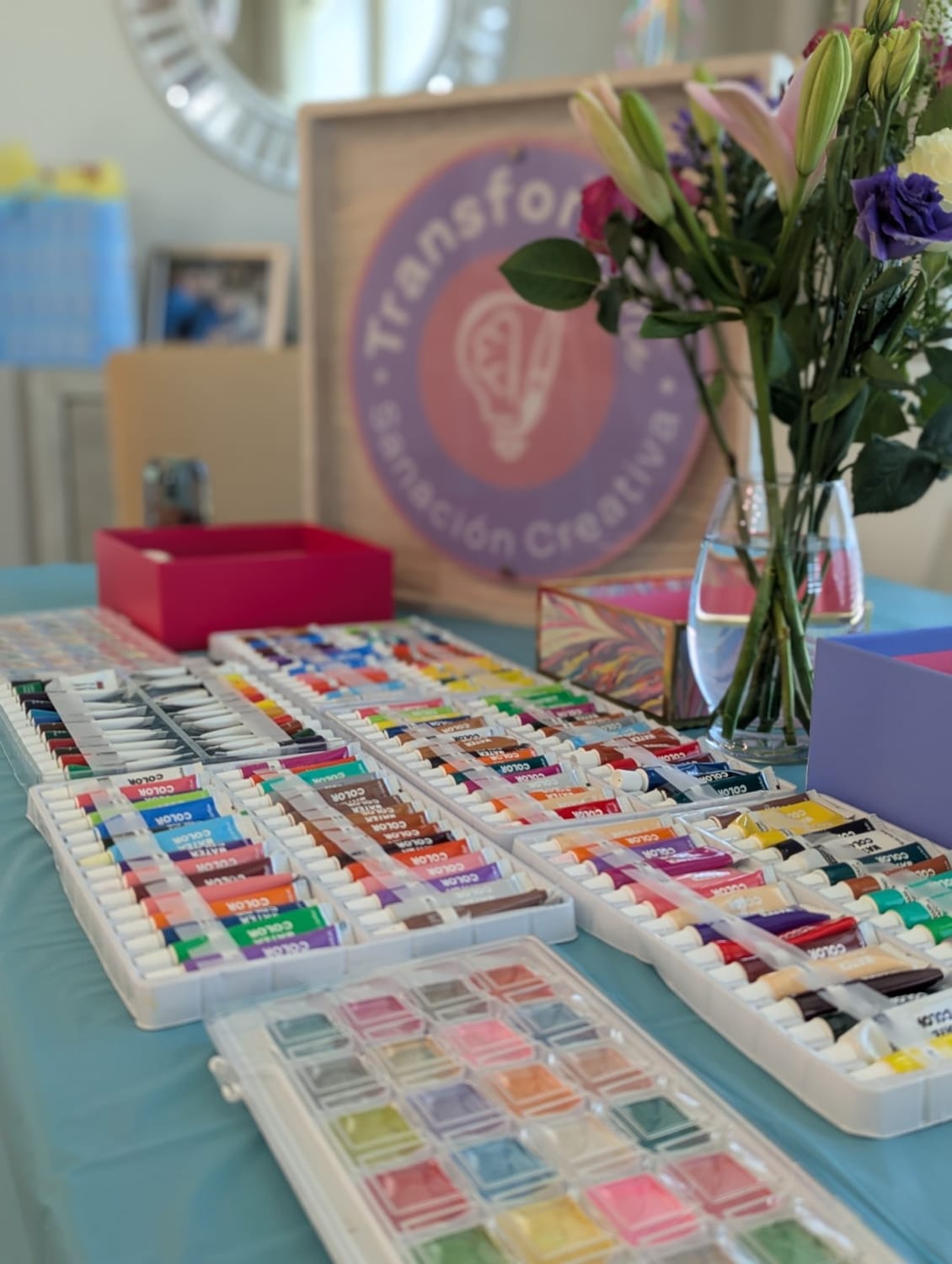 Materiales artísticos, flores y letrero de TransformArte preparados para un taller