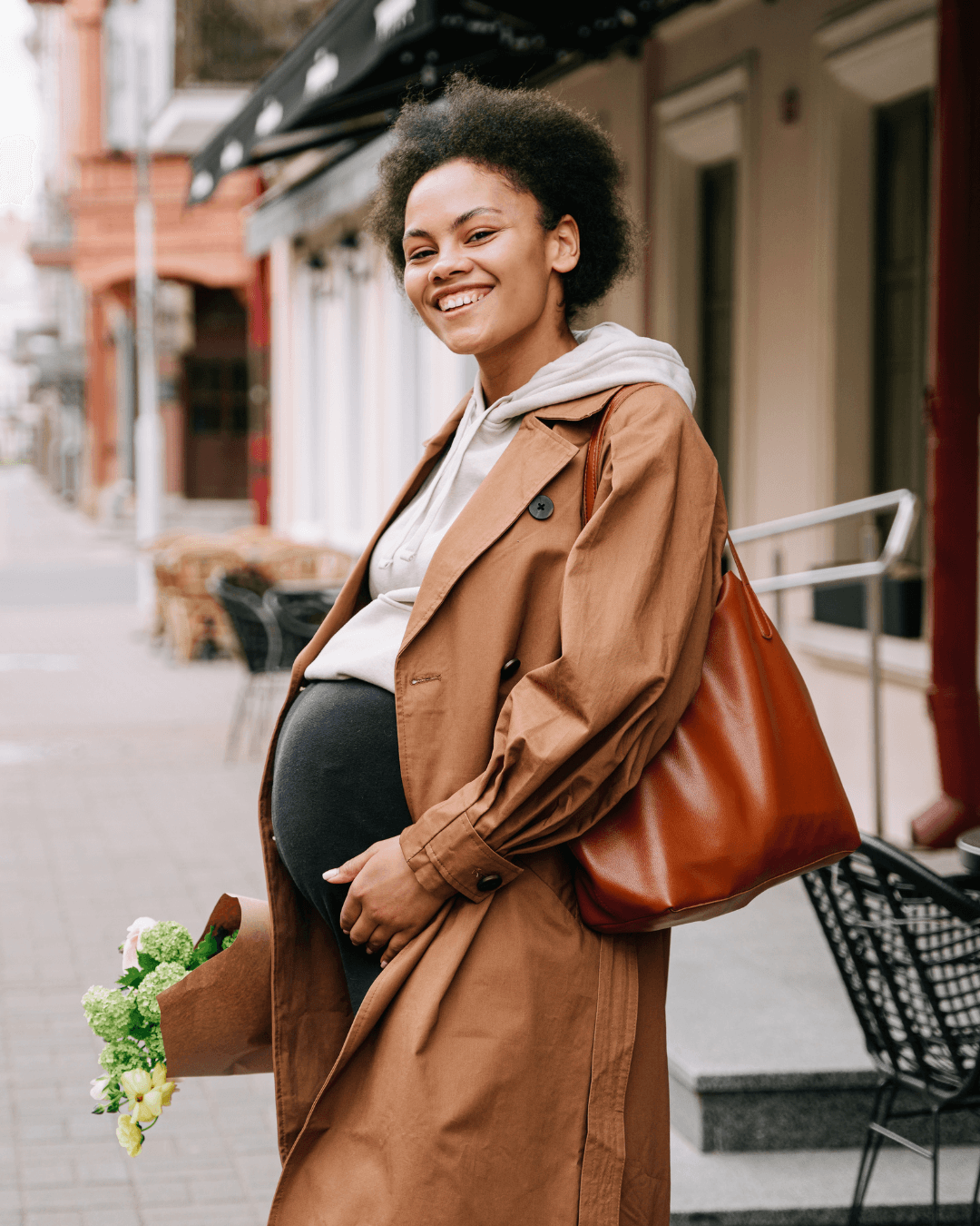 pregnant black woman standing on street holding a bunch of flowers and smiling