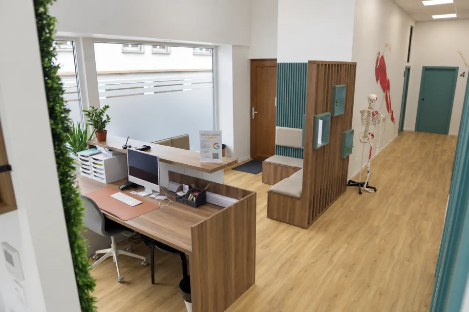L'accueil du cabinet Kiné Prévert à Strasbourg : comptoir en bois vu de côté, banquettes, claustra et couloir vers les salles