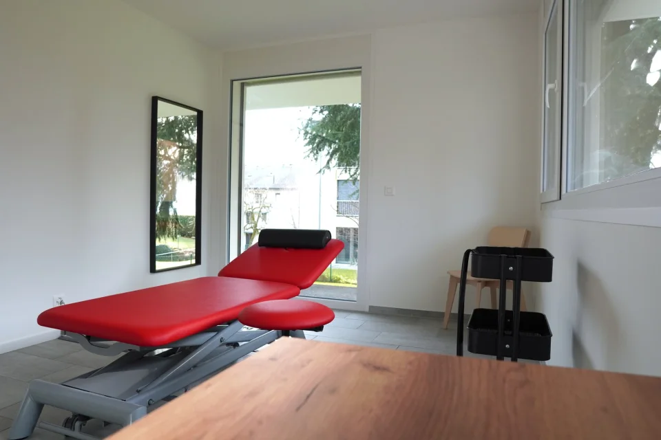 Une salle de soin de SwissCab Physio, table rouge et grande fenêtre