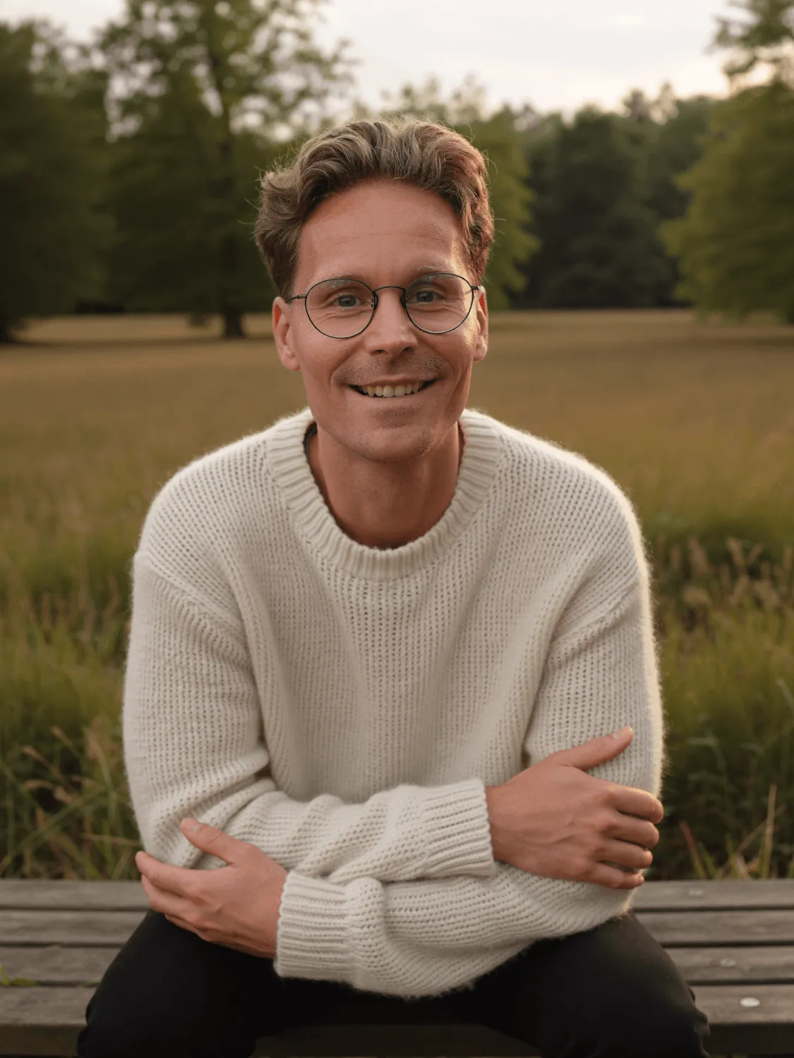 Daniel Müller auf einer Holzbank am Wiesenrand im Abendlicht